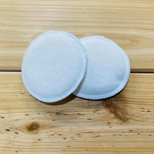 Two white microfiber applicator pads on a wooden surface.