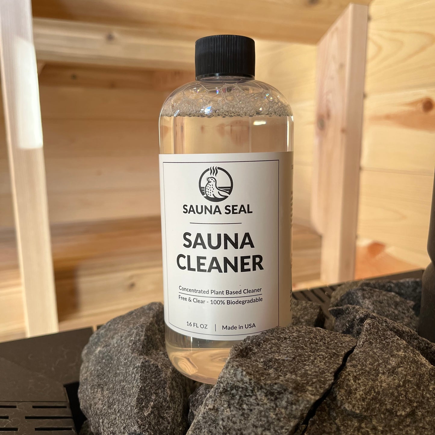 clear bottle with white label sitting on sauna stove rocks