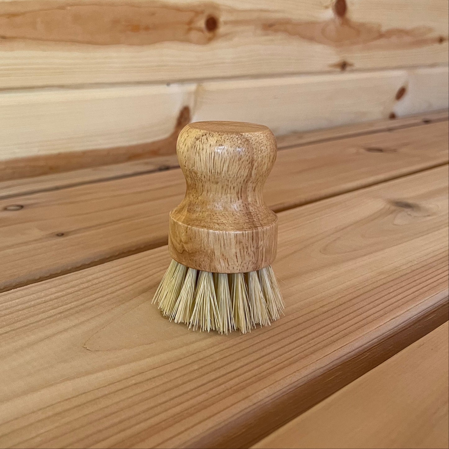 A scrub brush with a wooden handle and natural fiber bristles, placed on a wooden surface.