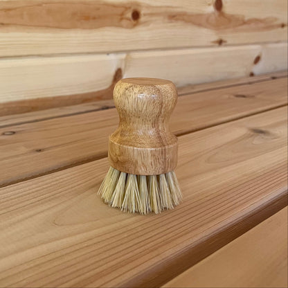 A scrub brush with a wooden handle and natural fiber bristles, placed on a wooden surface.